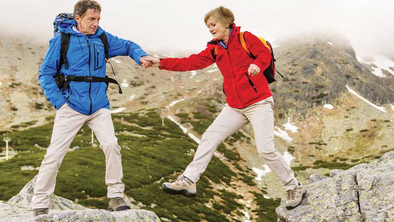 Man helping his wife walk across a gap while hiking